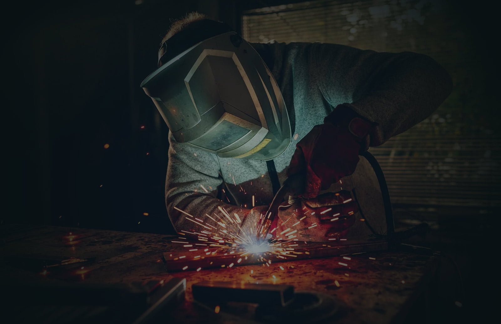 Un soudeur professionnel en action, portant un masque de soudage et des gants, travaillant sur une pièce métallique.